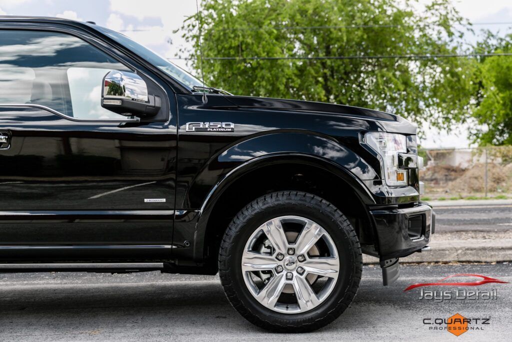 Black Ford F-150 truck with chrome wheels parked on pavement, bright sunny day.