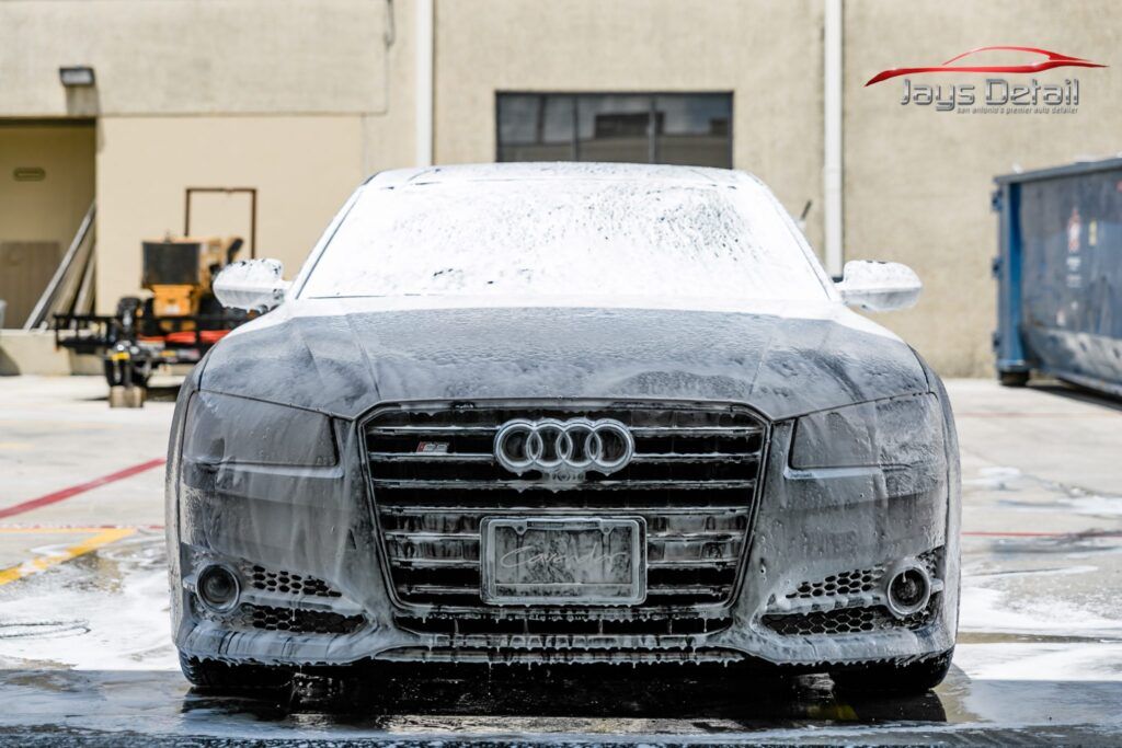 Audi covered in white foam during a car wash, in front of a building.