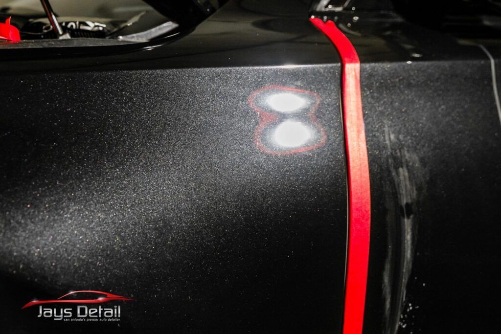 Black car surface with tape, showing before/after polishing results, two spots highlighted.