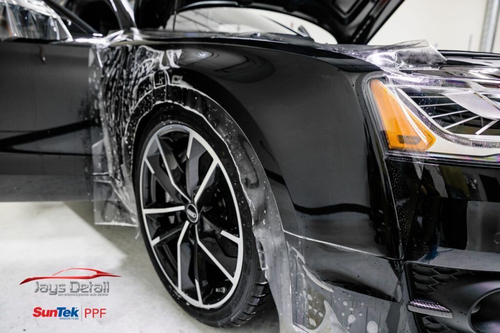 Black car getting paint protection film applied; detailing shop.