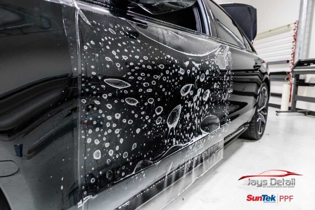 Black car with clear protective film applied to the side. Bubbles are visible under the film.