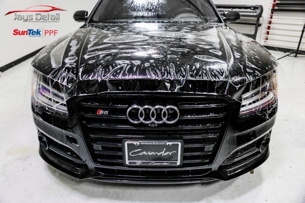 Black Audi car being coated with a protective film in a garage.