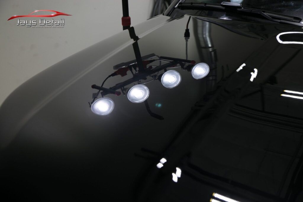 Black car hood with bright lights illuminating the surface, showing reflections.