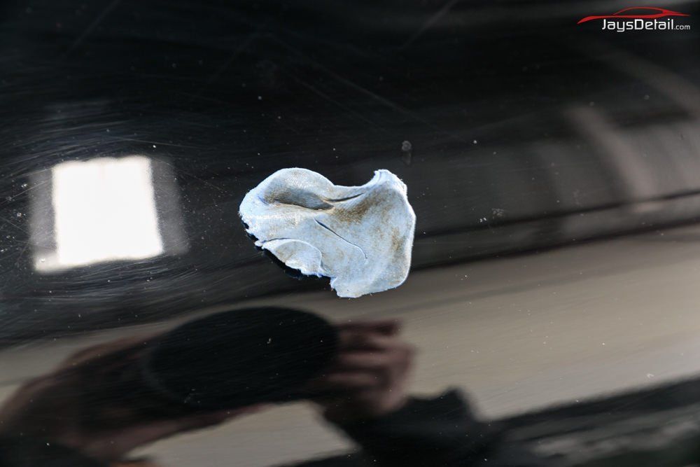 A dirty, wadded-up cloth on a black car's surface; a person is reflecting in the paint, holding an object.