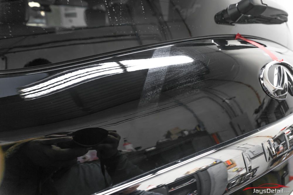 Black car trunk with scratches, reflection of a room, chrome accents and Acura logo.