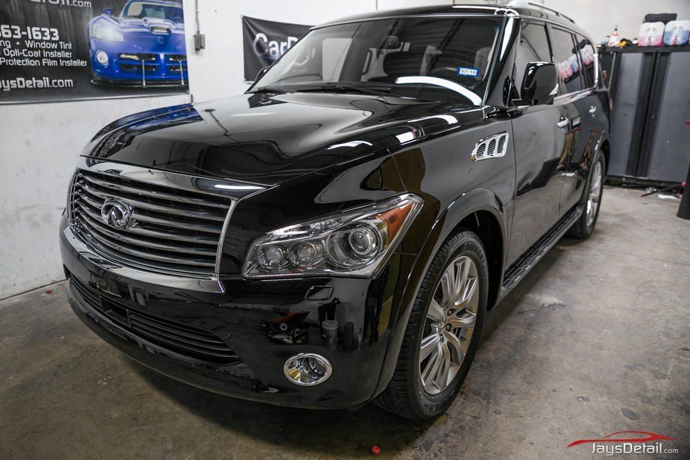 Black Infiniti QX80 SUV, shiny exterior, chrome grill, parked indoors.