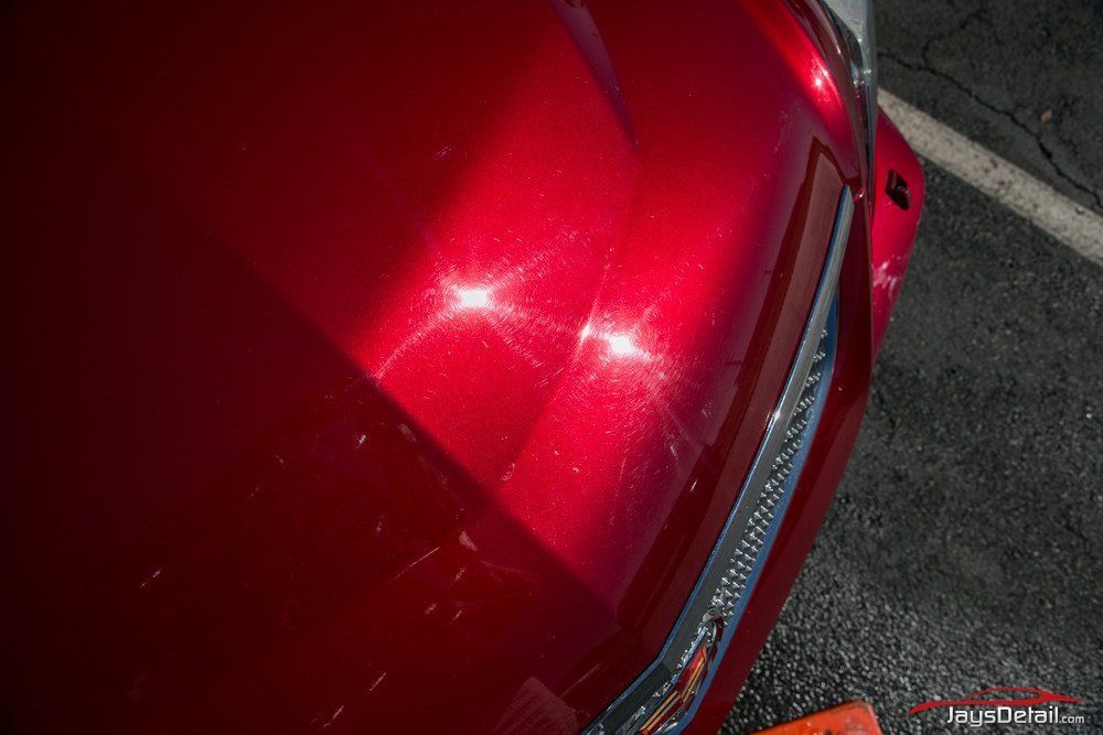 Red car hood reflecting sunlight, with two bright starburst reflections.