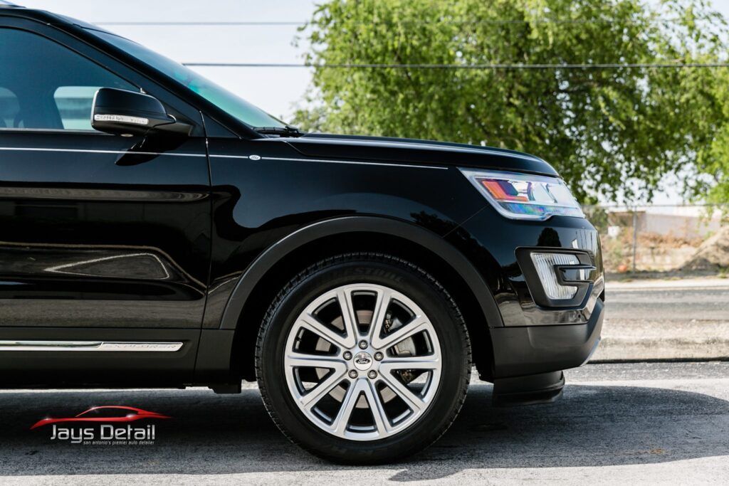 Black Ford Explorer SUV parked on a road. Chrome wheels, bright headlights, and a tree in the background.
