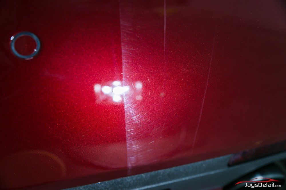 Red Corvette rear end, taillights illuminated. Shiny paint, outdoor setting.