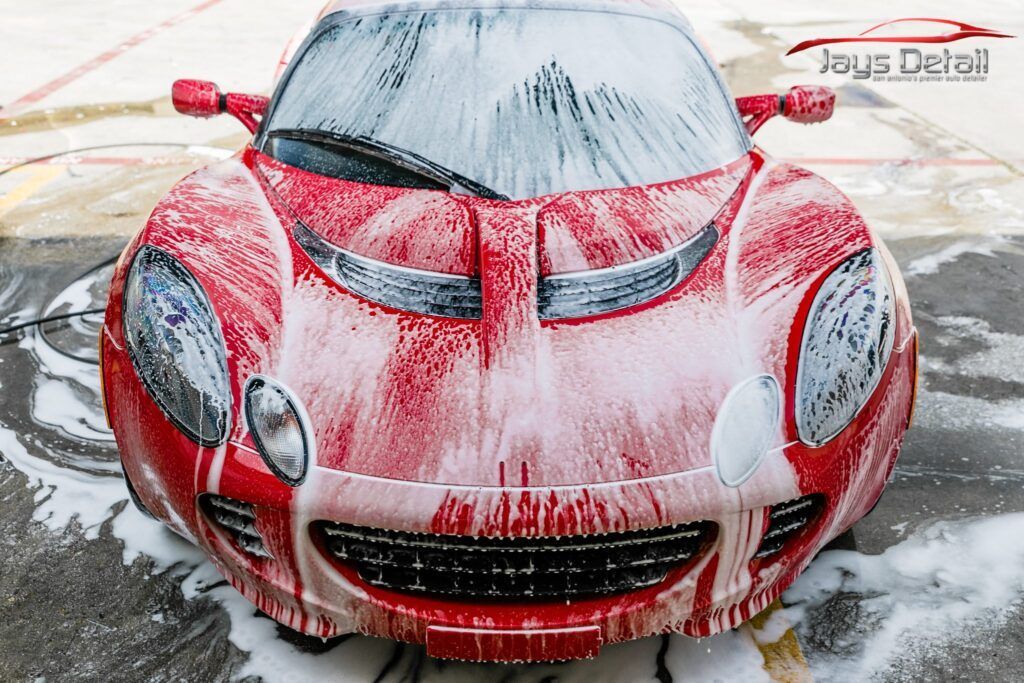 Red sports car covered in white foam, being washed.
