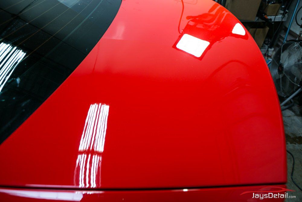Glossy red car roof reflecting bright lights and a window.