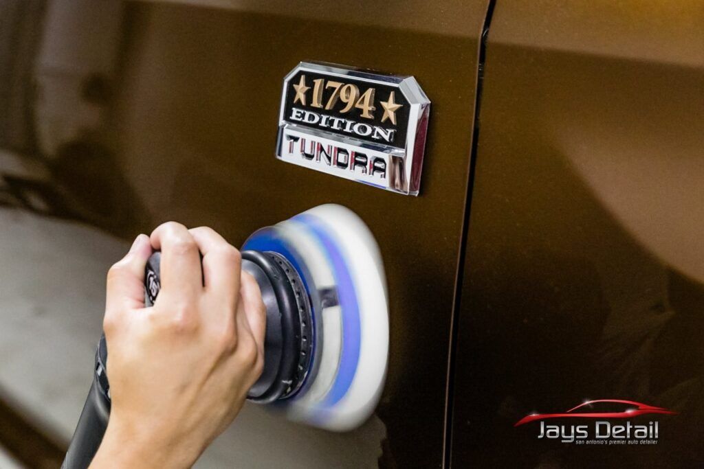 Person polishing a brown Toyota Tundra with a buffer near the