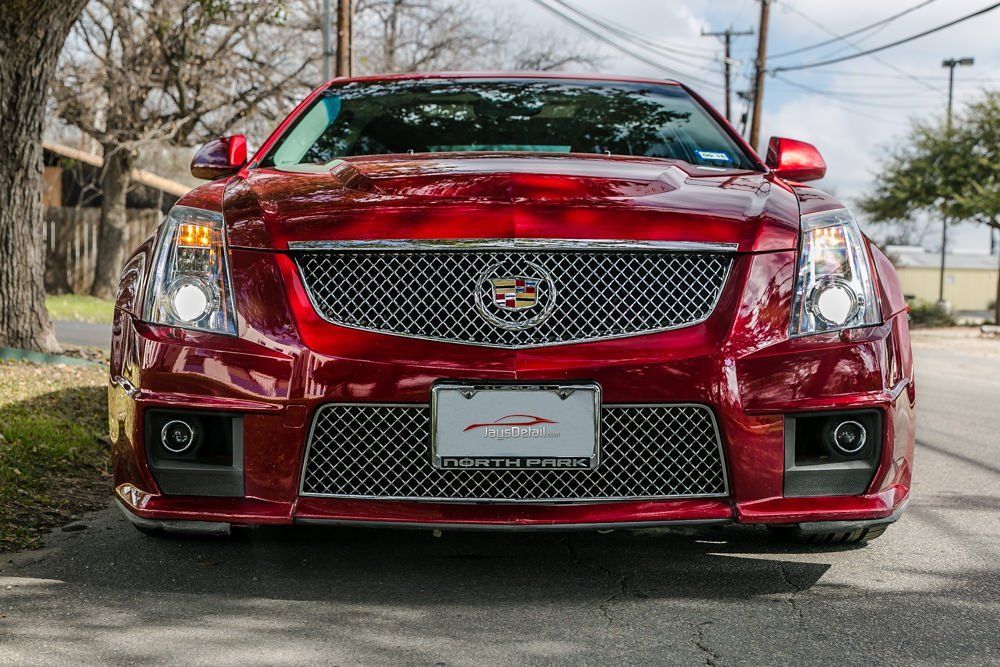 Red Cadillac CTS-V parked on a street; front view with chrome grill and headlights.