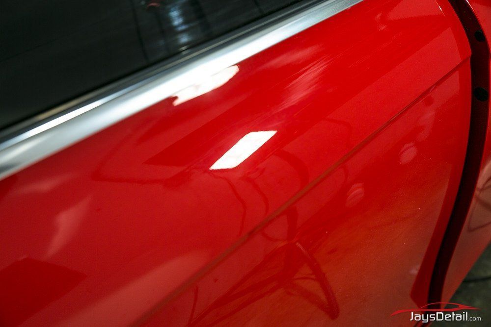 Red car door reflecting light, with chrome trim along the top edge.