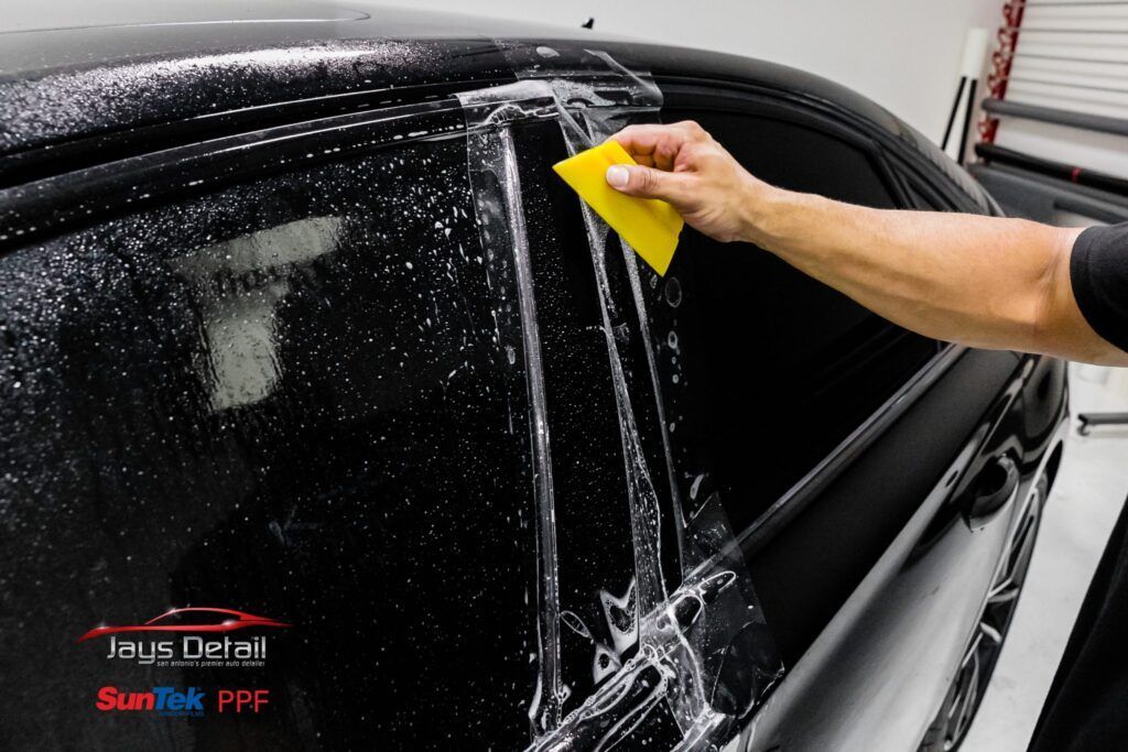 Person applying tint to a car window with a squeegee, in a shop setting.
