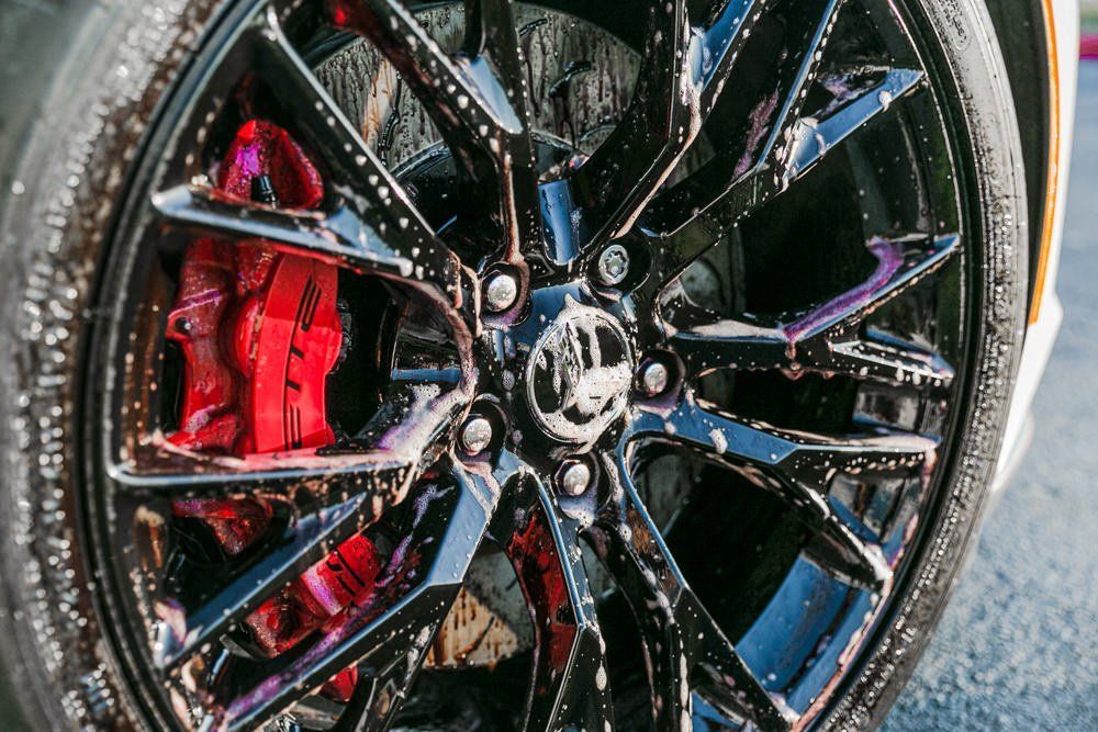 Black car wheel being washed with red brake calipers.