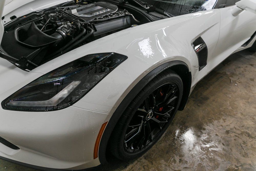 White sports car with black wheels and open hood.