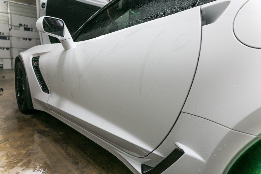 White sports car with the hood open and water droplets on the side.
