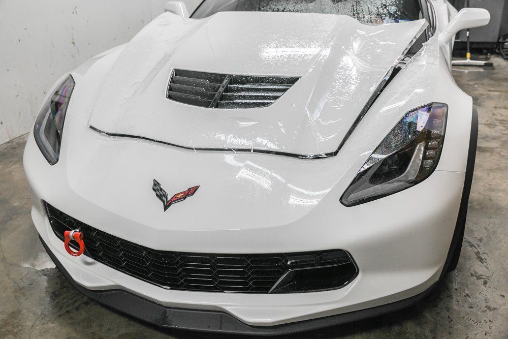 White Corvette covered in soap, front view. Red tow hook visible.