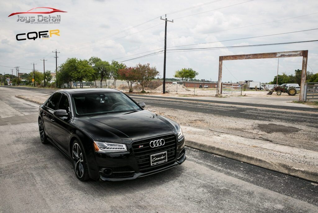 Black Audi S8 parked on the side of a road with an open frame in the background. Cloudy day.