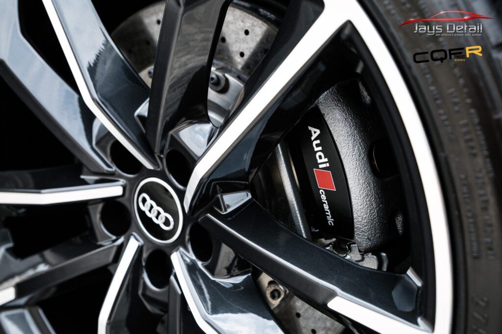 Close-up of a black Audi RS brake caliper and wheel, with the Audi logo prominently displayed.