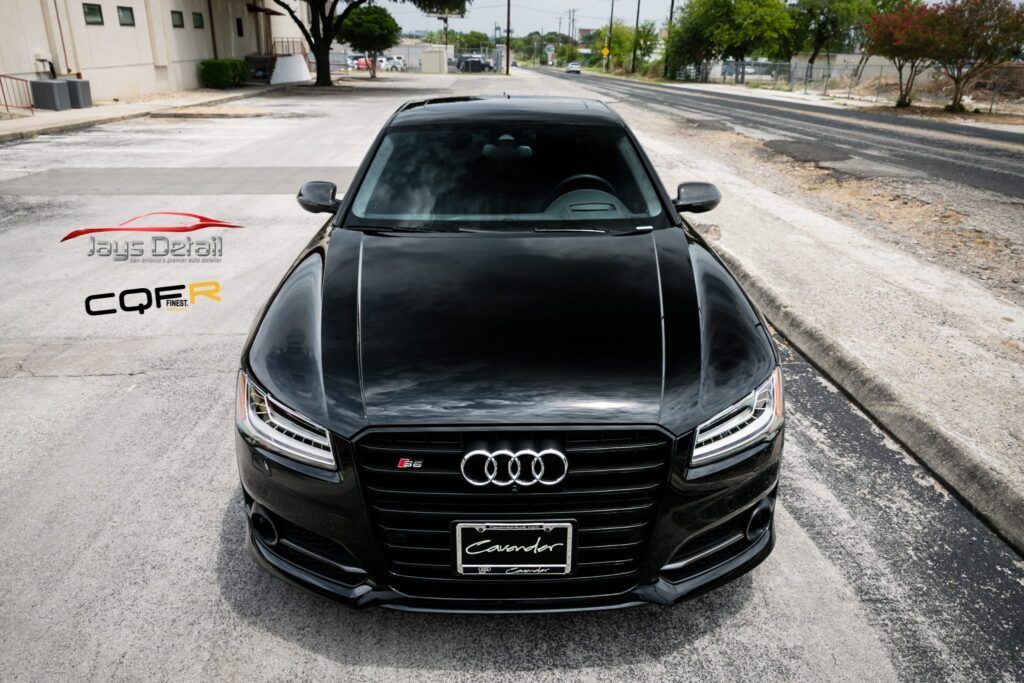 Black Audi S8, front view, parked on a street with commercial buildings in the background.