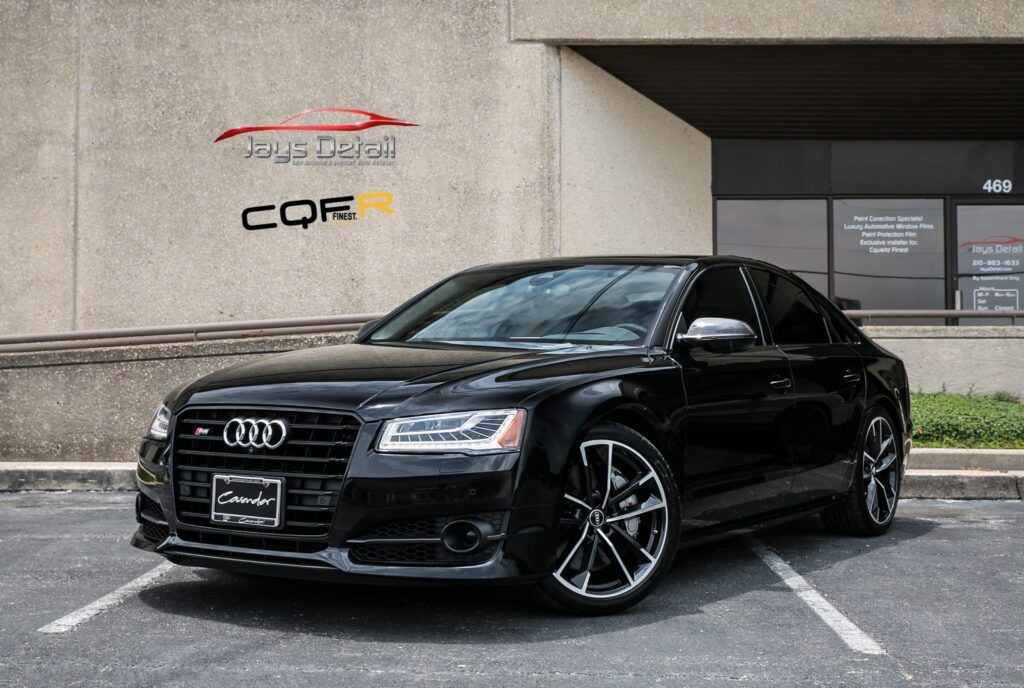 Black Audi S8 sedan parked in front of a building with logos on the wall.