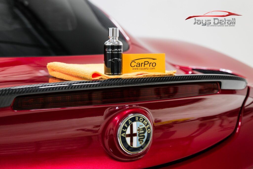 Car detailing products on a red Alfa Romeo hood, with logo and carbon fiber accents.