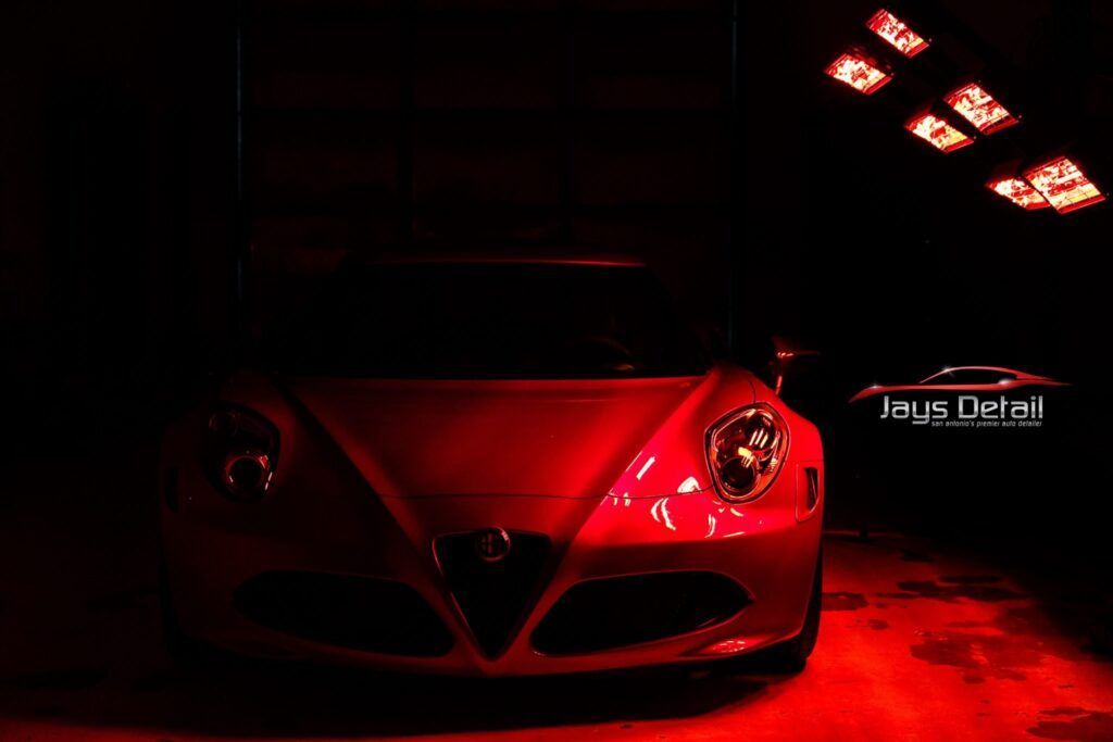 Red sports car under red lights in a dark garage.