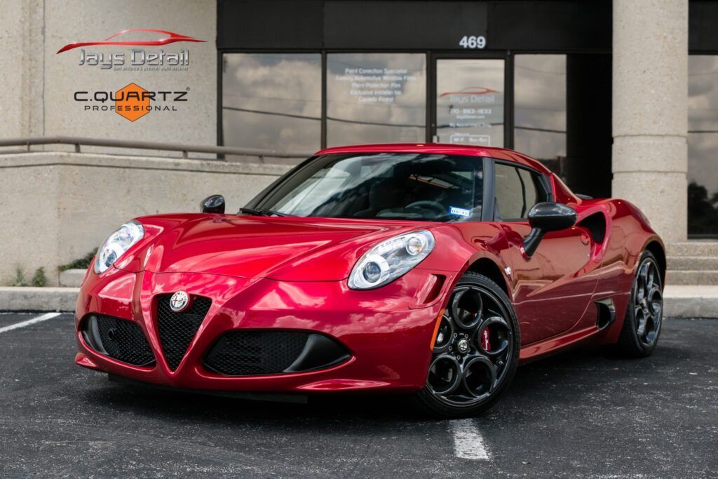 Red Alfa Romeo 4C sports car parked in front of a building with black wheels and a black grille.