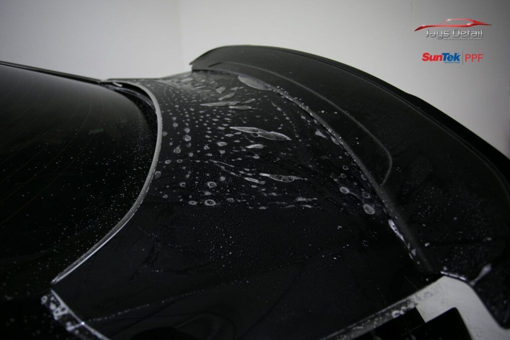 Black car with water droplets on a spoiler and rear window. Close-up, indoor shot.