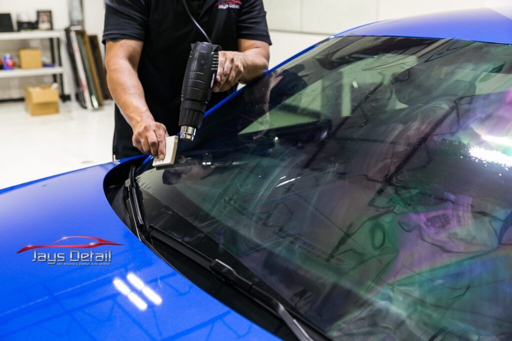A person applying tint to a blue car's windshield with a heat gun.