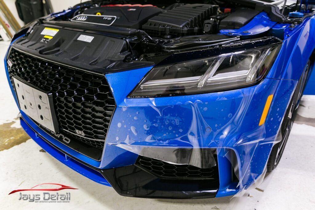 Blue Audi TT with protective film on the front, detailing work, black grill, indoor setting.