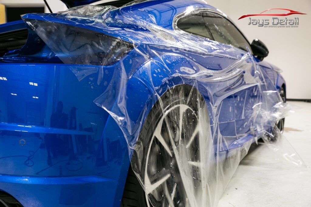 Blue car being wrapped with protective film in a garage.