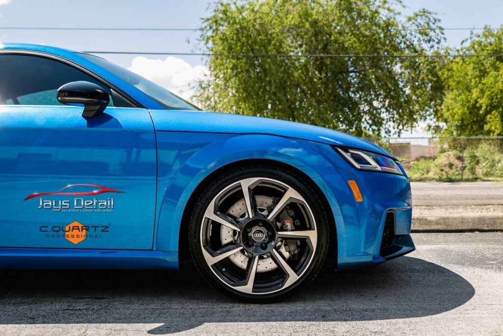 Blue Audi TT RS, parked outdoors, with custom wheels and logo on the side.