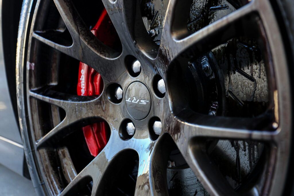 Close-up of a glossy black car wheel with red brake calipers; a black center cap has a logo.