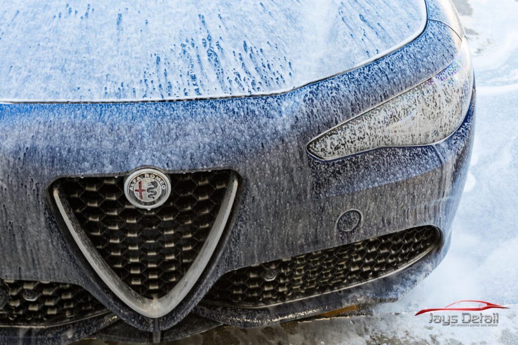 Frozen blue Alfa Romeo front end; emblem, headlights, grille, and sensors visible. Snow and ice coverage.