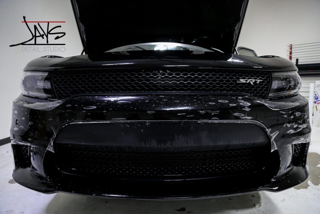 Black car with open hood, showing front grille and bumper.