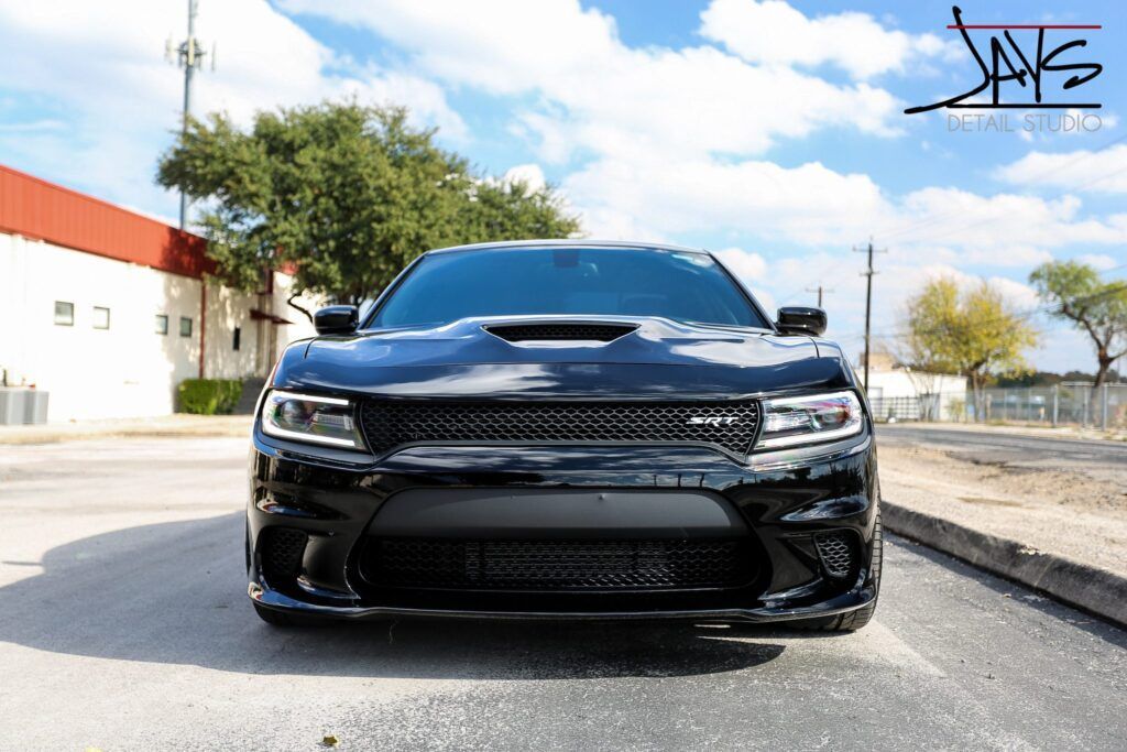 Black Dodge Charger on asphalt, front view. Cloudy sky, building backdrop,