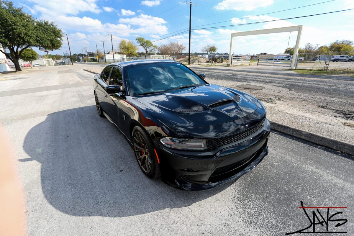 Black Dodge Charger parked on asphalt under a bright blue sky.