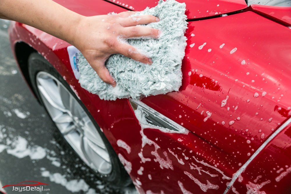 Hand washing a red car with a sudsy mitt; silver wheel visible.