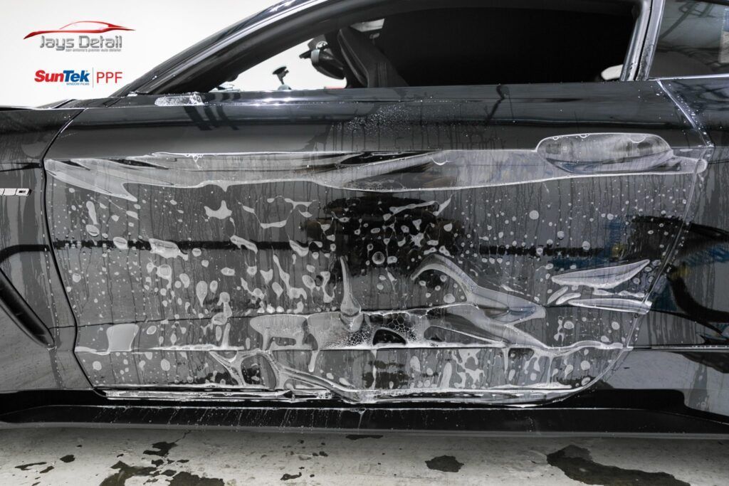 Car with protective film applied, covered in suds. Garage setting.