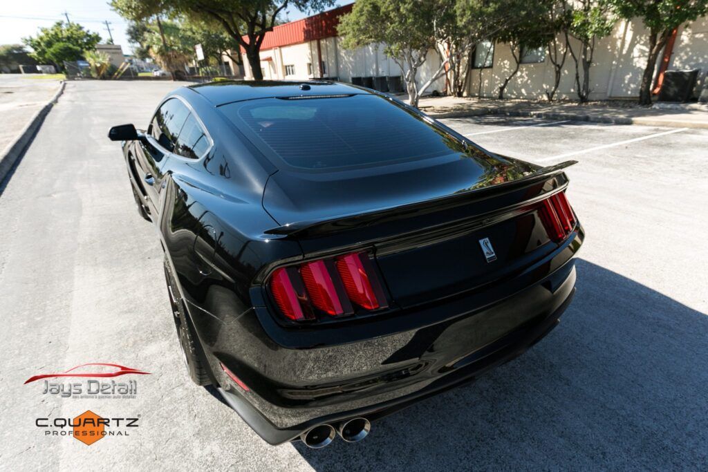 Black Ford Mustang parked on asphalt, rear view, sunny day.