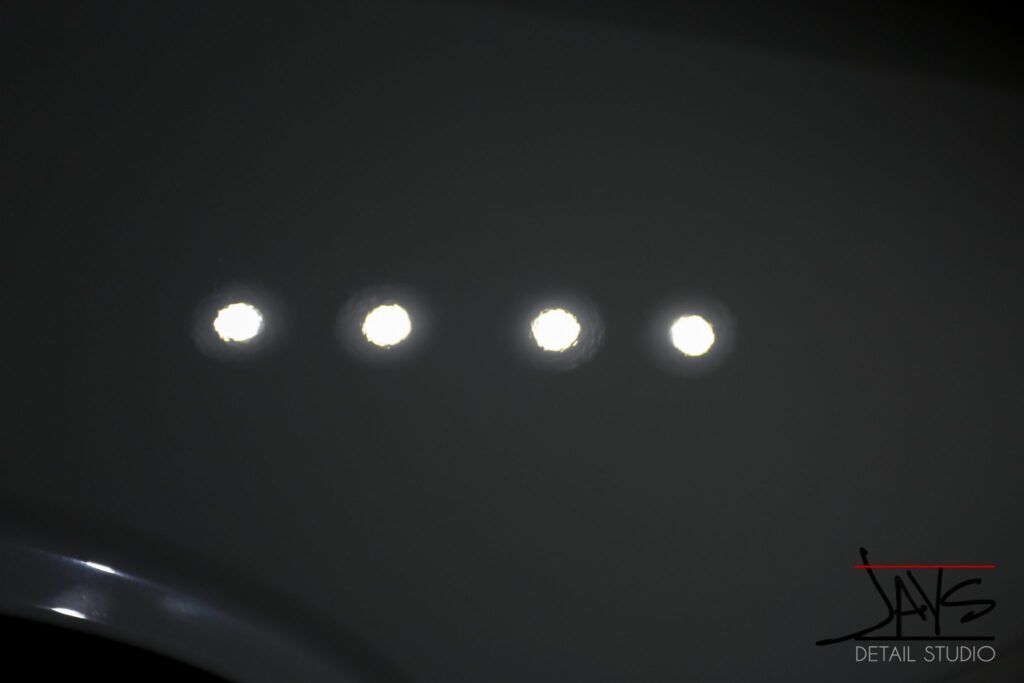 Four bright lights reflected on a grey car's surface.