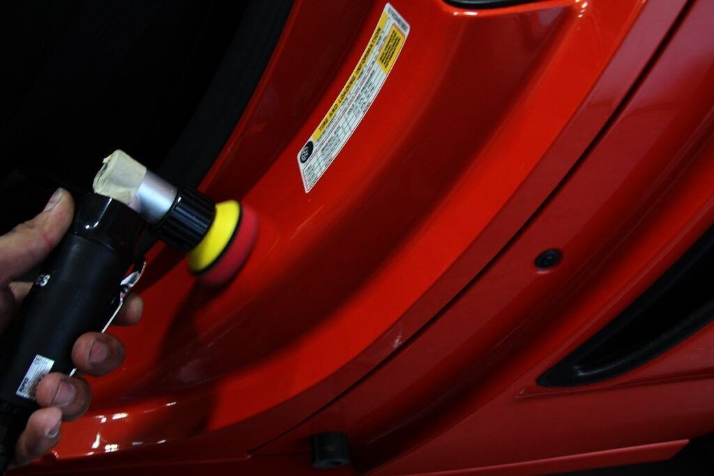 Hand polishing a red car door with a small rotary polisher.