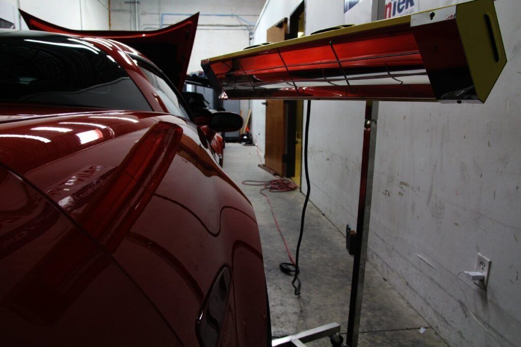 Red car being heated with infrared lamp in a body shop.