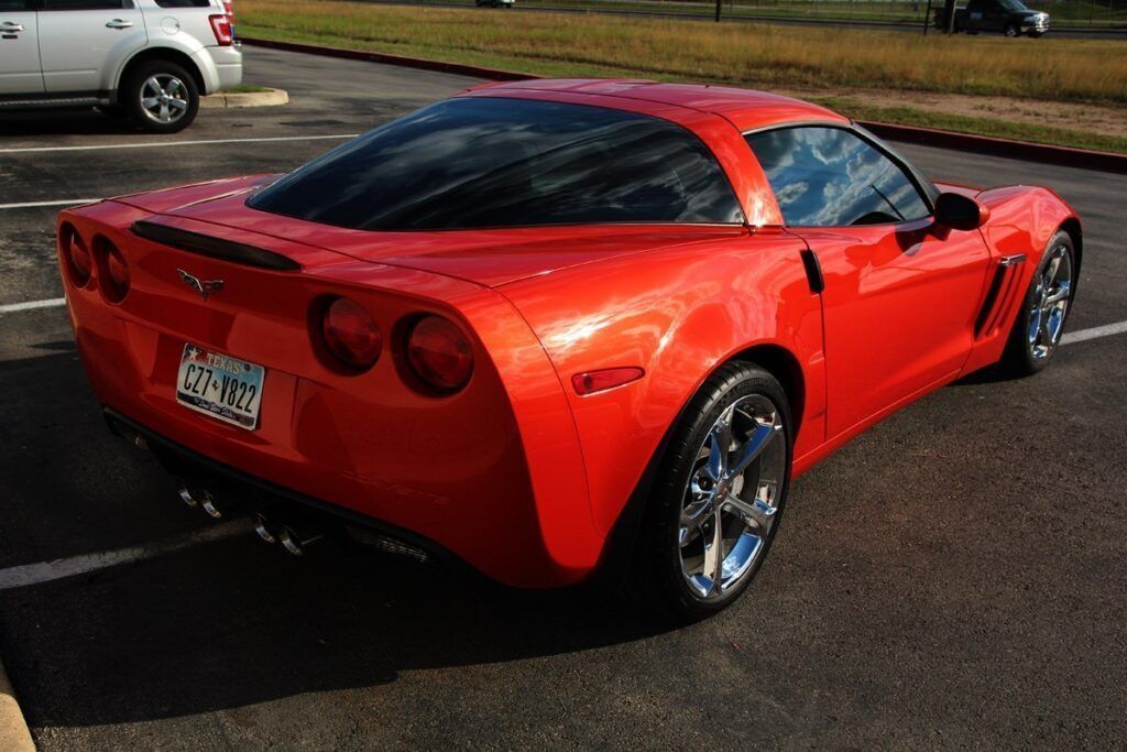 Red Corvette sports car parked in a parking lot, angled view from the rear.