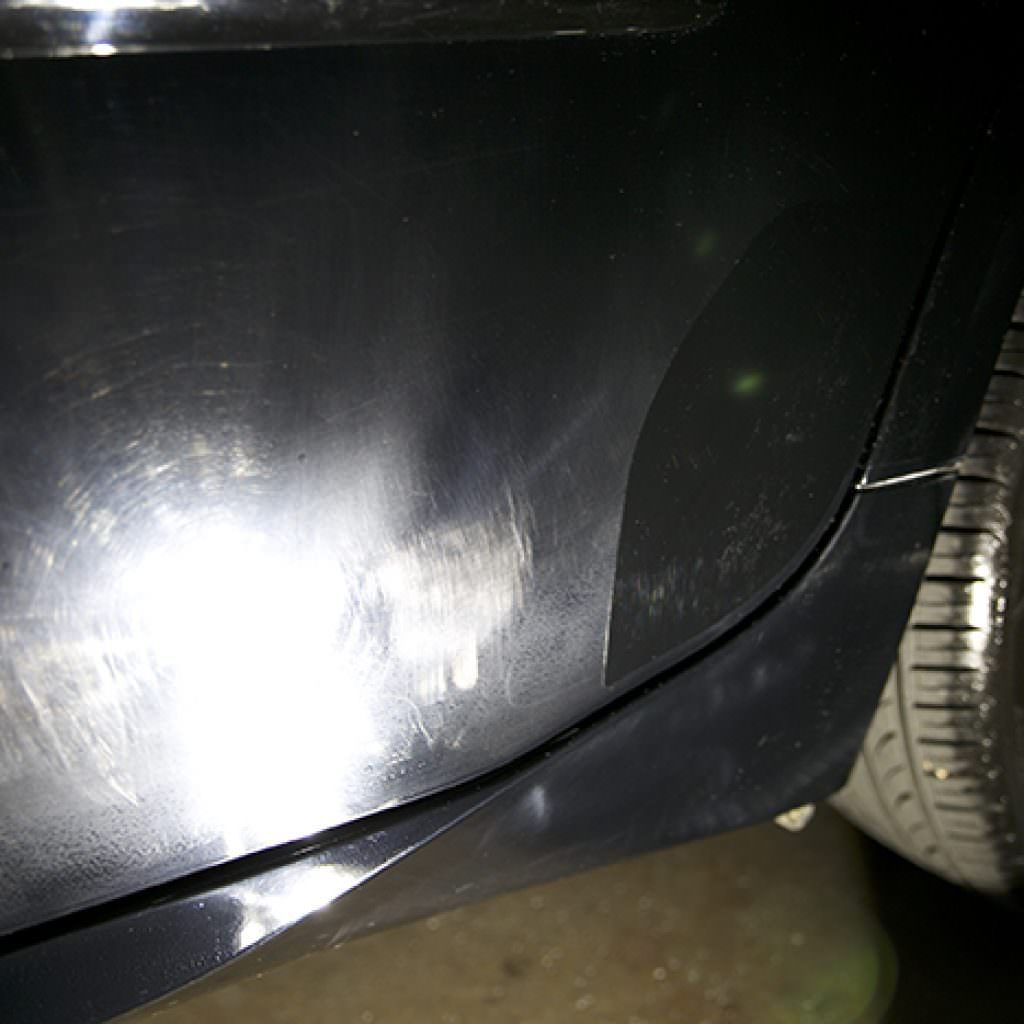 Black car bumper with scratches and a detached section, next to a tire.