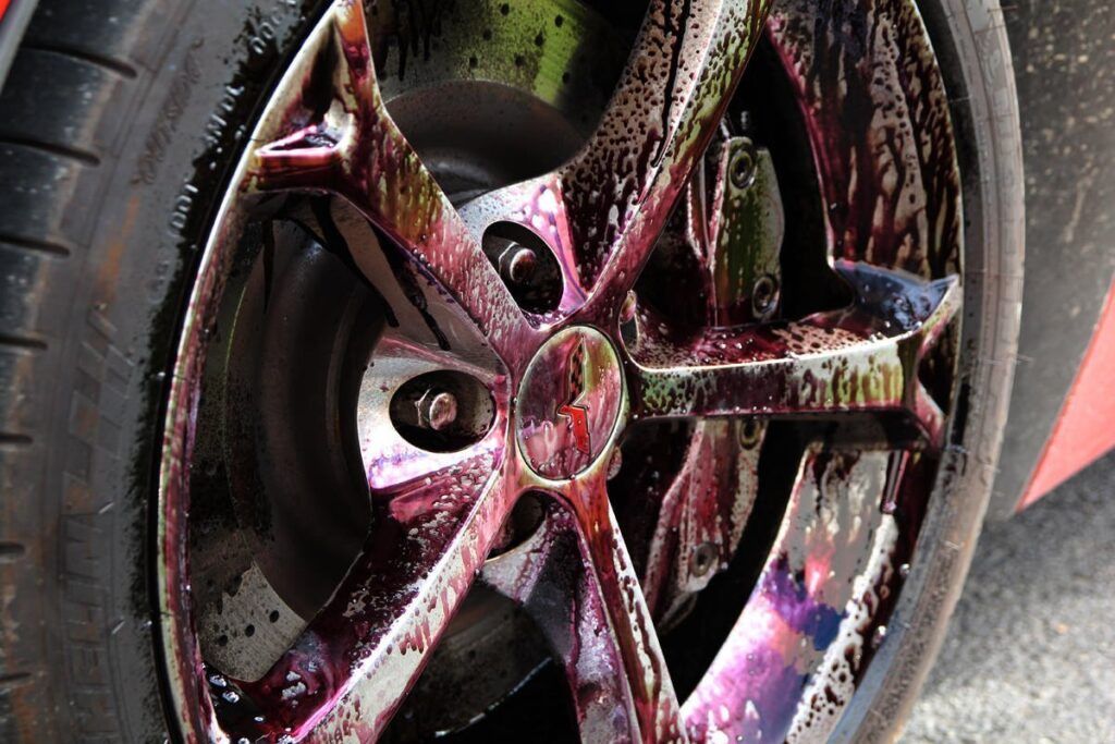 Car wheel being cleaned with a purple iron remover spray.