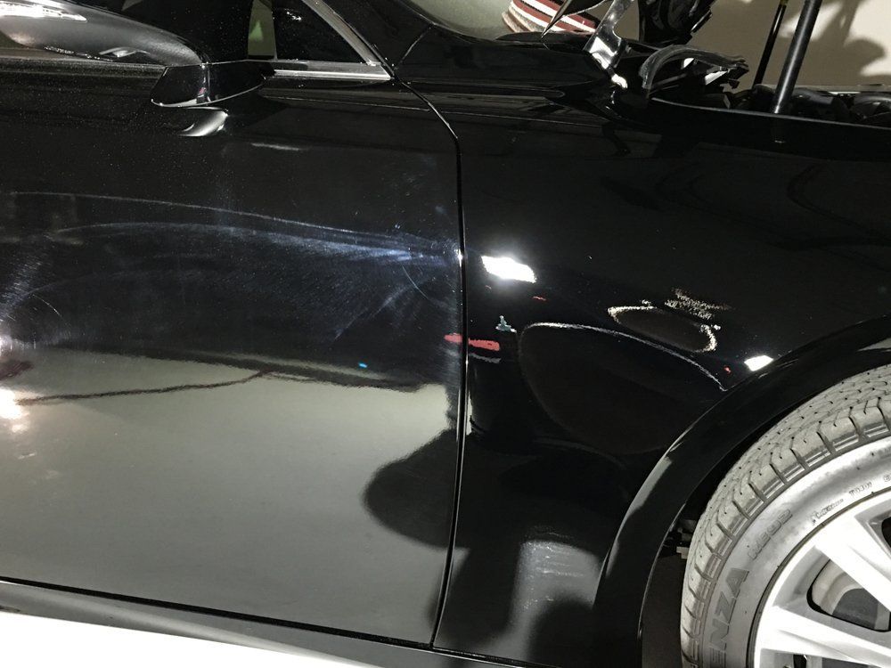 Black car with scratches on the side panel, likely from an accident.